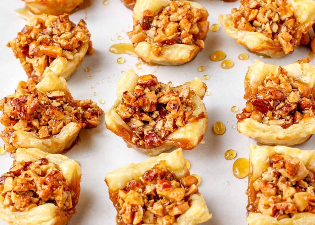 Puff pastry cups on parchment, filled with nuts and drizzled with honey 