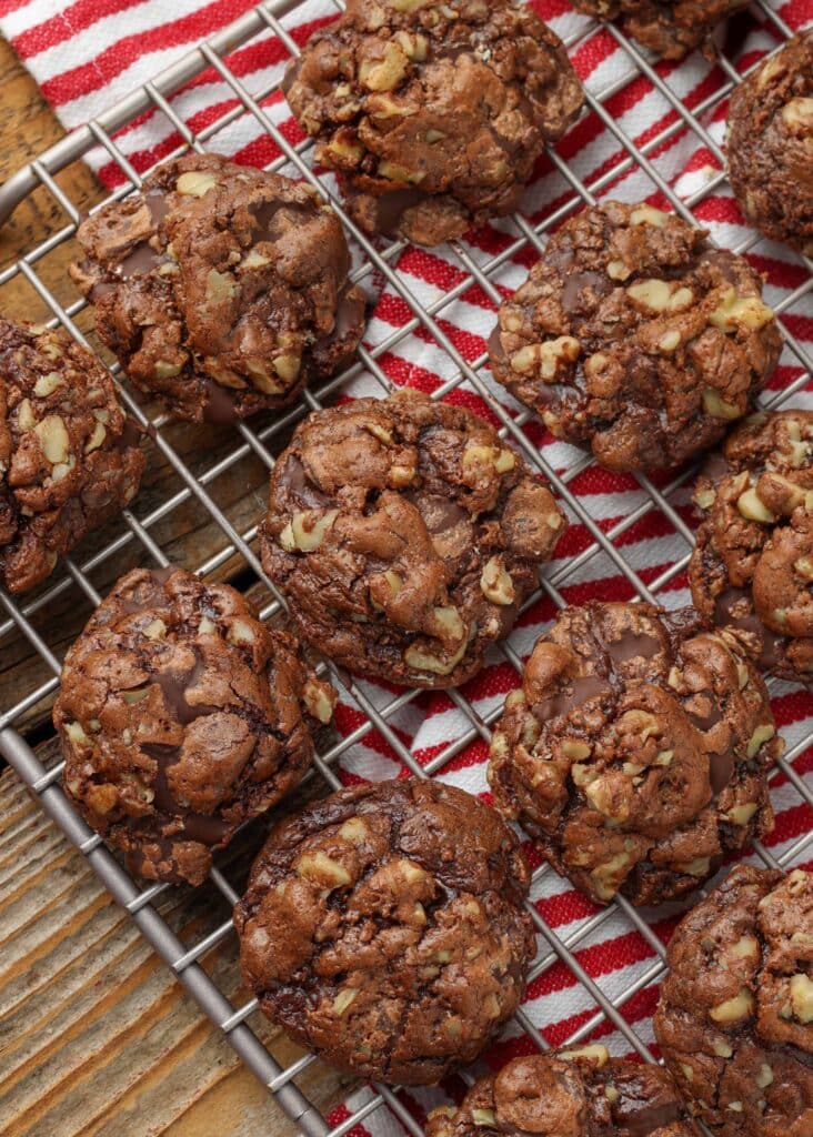Overhead vertical shot of chocolate walnut cookies on a silver cooling rack; underneath, a striped red and white hand towel