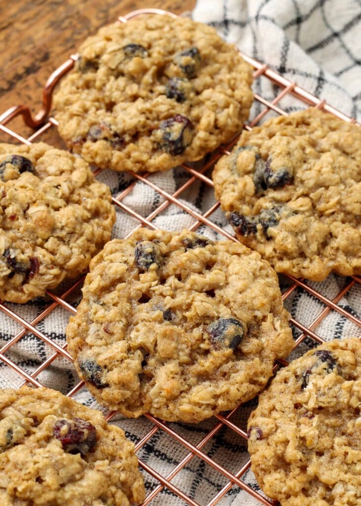 Overhead close-up vertical shot of cranberry orange oatmeal cookies on a copper cooling rack; underneath, a checkered white and black hand towel