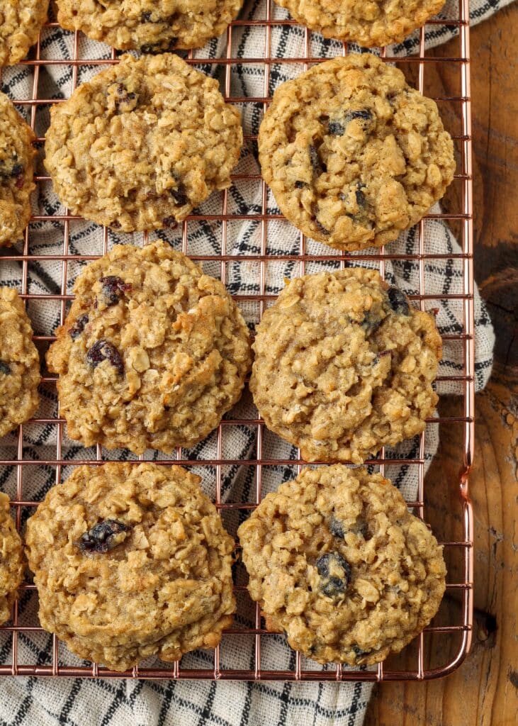 Overhead shot of cranberry orange oatmeal cookies on a copper cooling rack; underneath, a checkered white and black hand towel