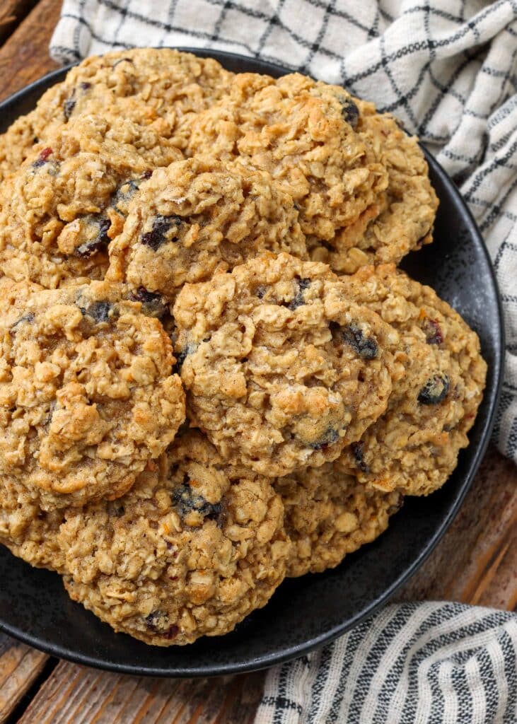 Overhead shot of cranberry orange oatmeal cookies, piled in a black bowl with a checkered white and black hand towel