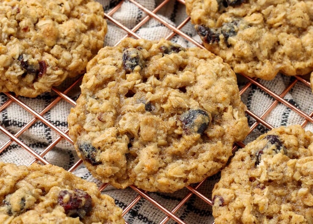 Overhead close-up shot of cranberry orange oatmeal cookies on a copper cooling rack; underneath, a checkered white and black hand towel