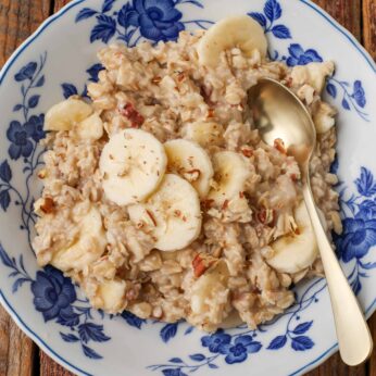 Overhead shot of maple banana nut oatmeal, served with a silver spoon in a white bowl with blue floral print