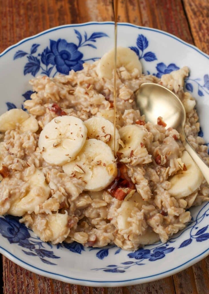 Overhead shot of maple banana nut oatmeal, served with a silver spoon in a white bowl with blue floral print