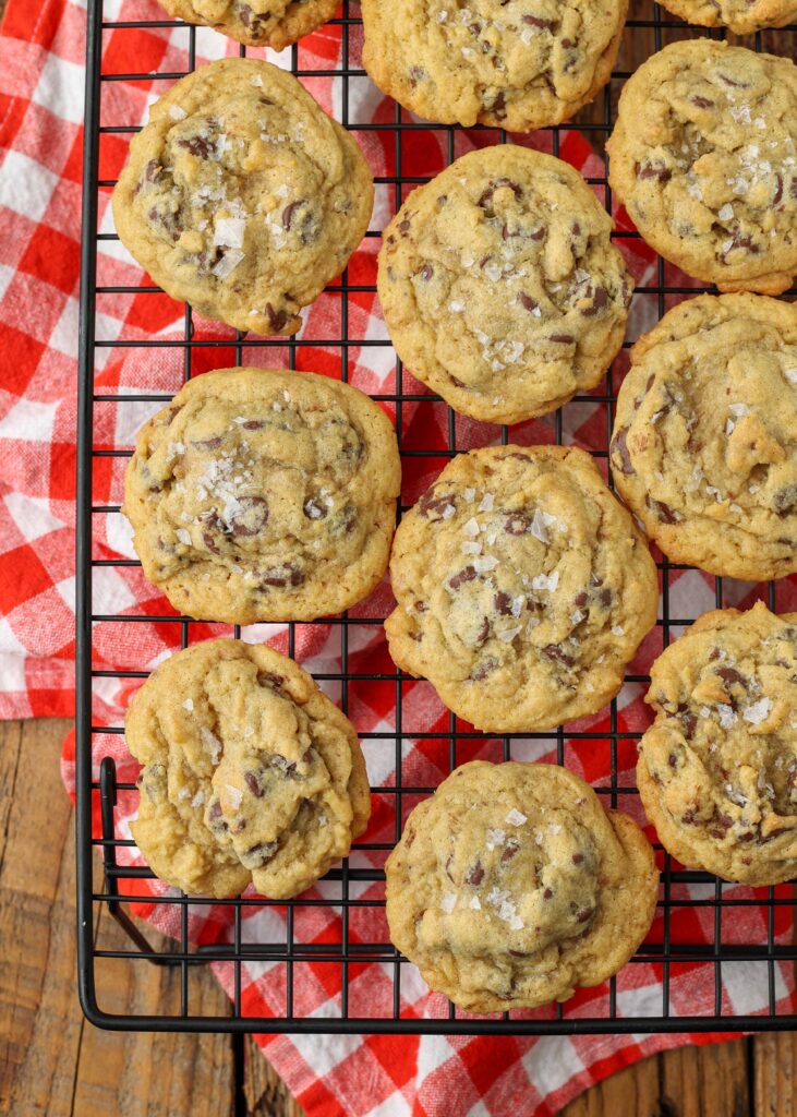 Overhead vertical shot of salted chocolate chip pudding cookies on a cooling rack; underneath the rack, a checkered red and white hand towel
