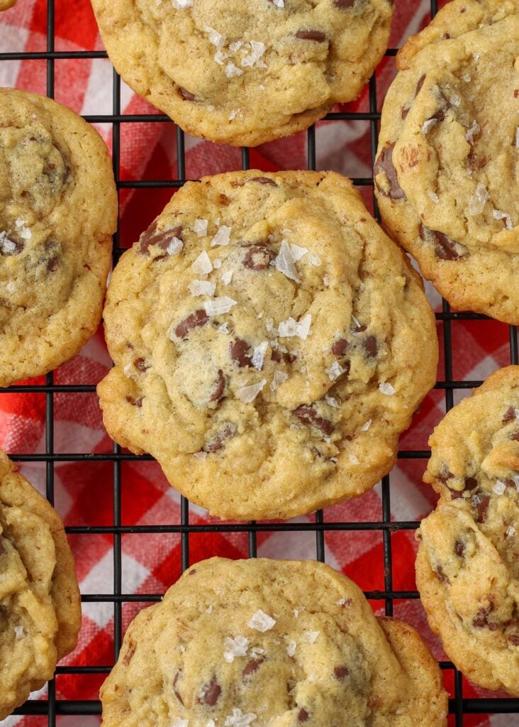 Overhead close-up shot of salted chocolate chip pudding cookies on a cooling rack; underneath the rack, a checkered red and white hand towel