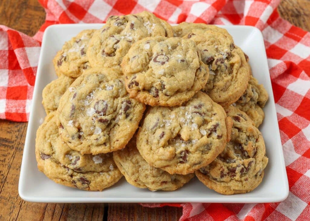 Overhead horizontal shot of salted chocolate chip pudding cookies, served in a white tray with a checkered red and white hand towel
