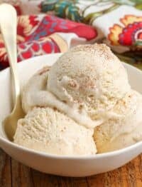 Vertical shot of cinnamon ice cream served in a white bowl with a floral hand towel and a gold spoon