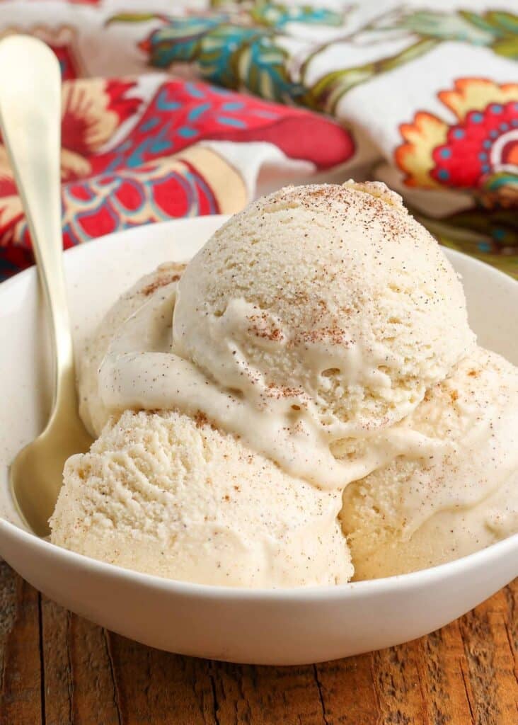 Vertical shot of cinnamon ice cream served in a white bowl with a floral hand towel and a gold spoon