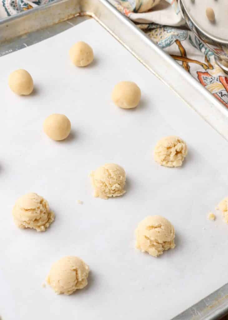 Scoops of almond butter cookie dough on a parchment paper lined sheet pan