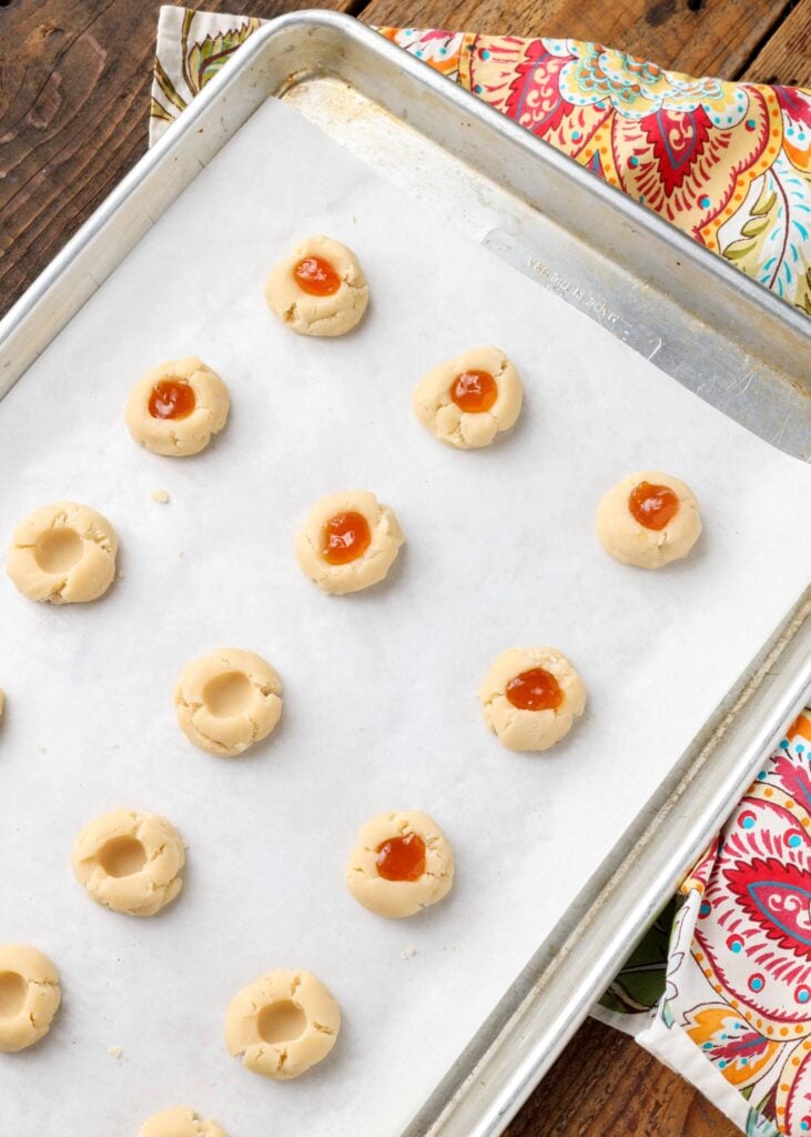 filling thumbrint cookies with jam on parchment tray