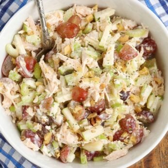 A top down photo of a white bowl filled with chicken waldorf salad, with a blue and white checkered napkin visible in the background.