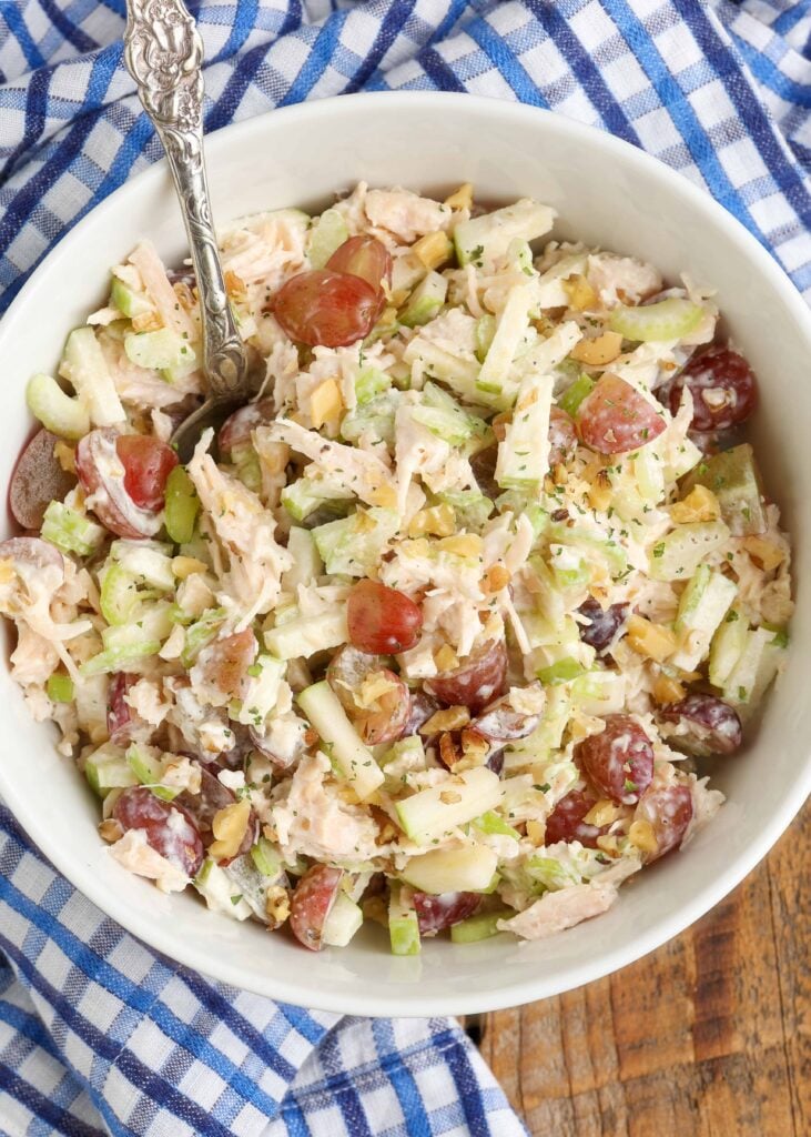 A top down photo of a white bowl filled with chicken waldorf salad, with a blue and white checkered napkin visible in the background.