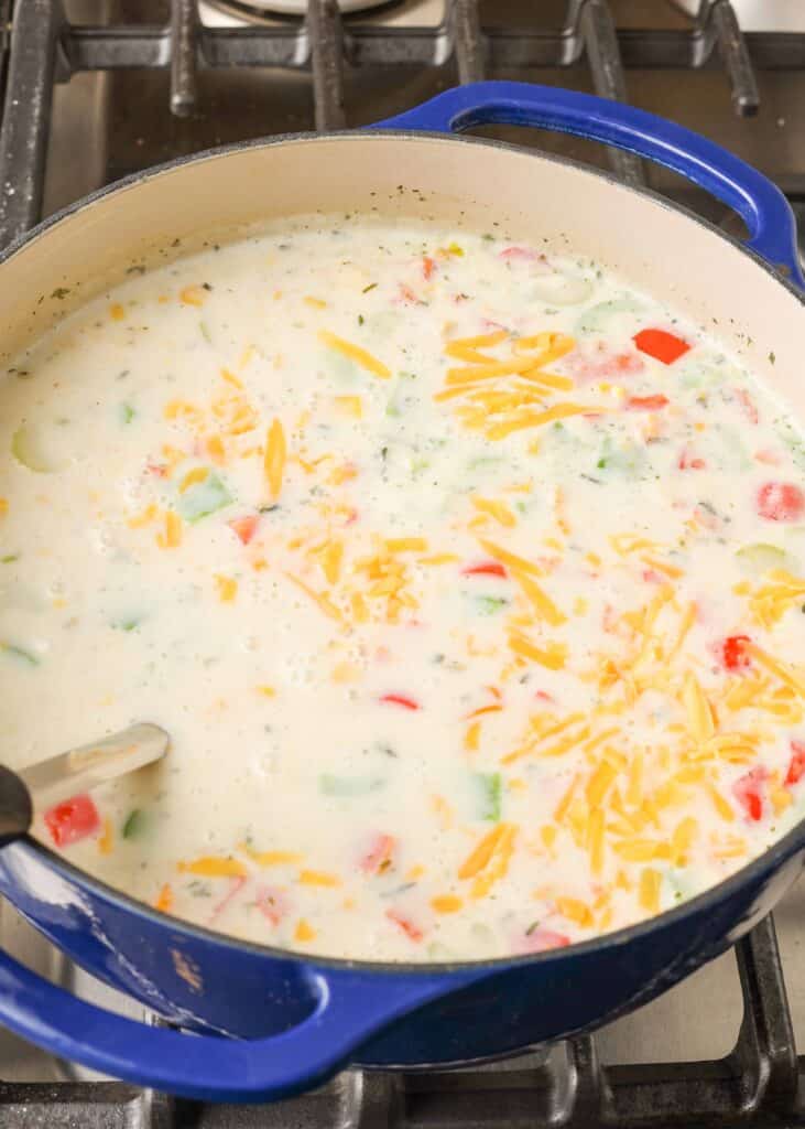 बर्तन में मलाईदार सब्जी सूप में पनीर मिलाया गया है, जो परोसने के लिए लगभग तैयार है।