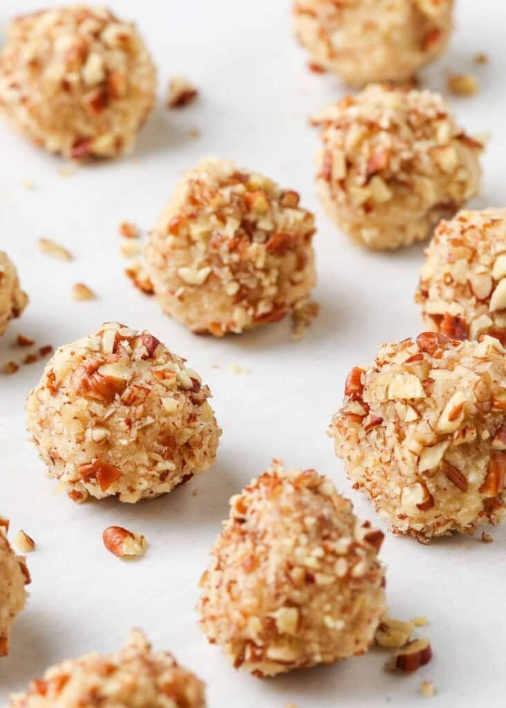 balls of dough on a white parchment paper, with pieces of pecans visible in the mix.