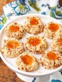 gluten free, jam-filled pecan thumbprint cookies are arrayed on a white serving dish over a colorful tea towel.