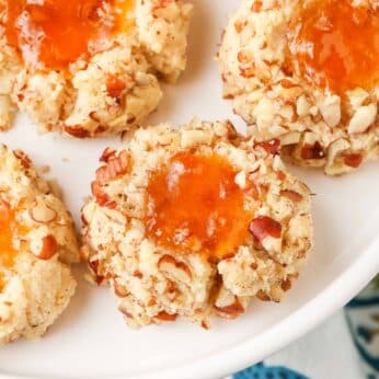 gluten free, jam-filled pecan thumbprint cookies are arrayed on a white plate.