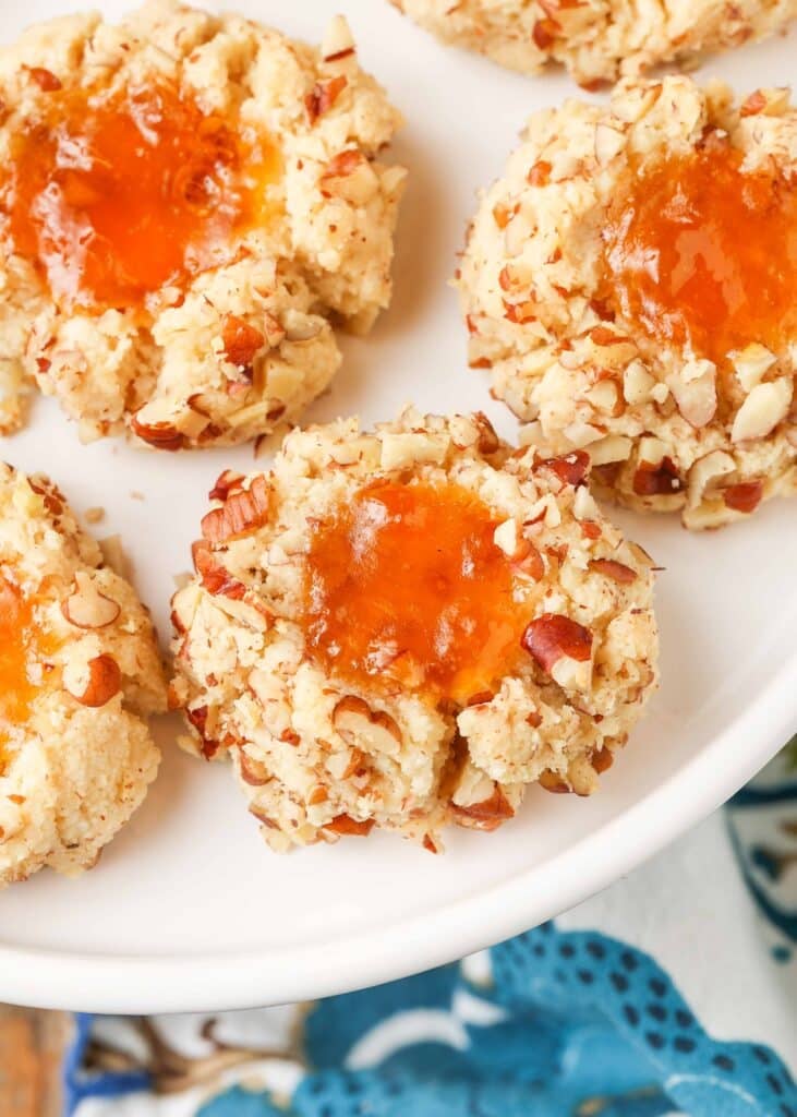 gluten free, jam-filled pecan thumbprint cookies are arrayed on a white plate.