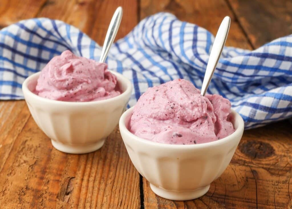 Close-up horizontal shot of pink ice cream in white bowls with silver spoons