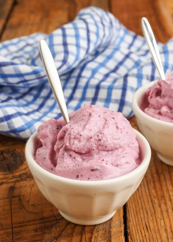 Pink soft serve ice cream in white bowls with silver spoons