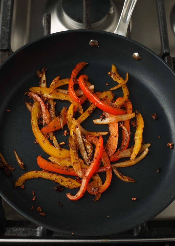 A top down shot of a black metal pan with sauteeing peppers and onions.