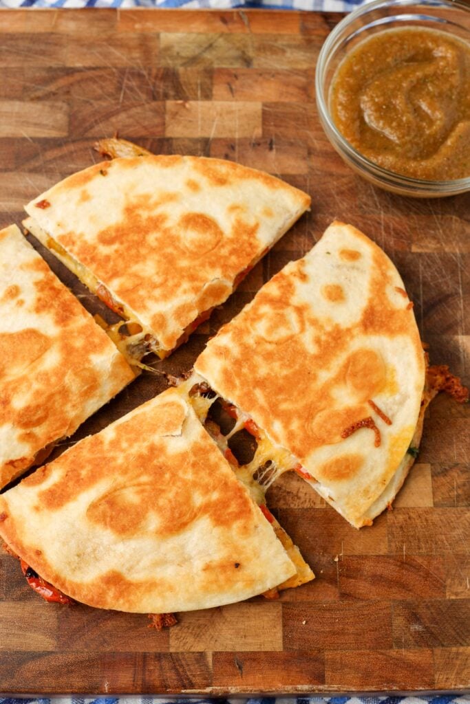 A vertically aligned photo of a sliced tortilla quesadilla in quarters on a wooden background.