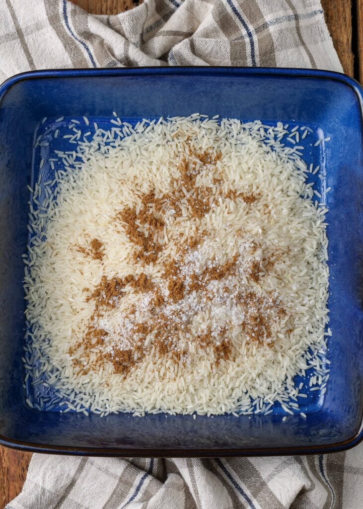 the rice has been seasoned in a blue baking dish, ready to stir.