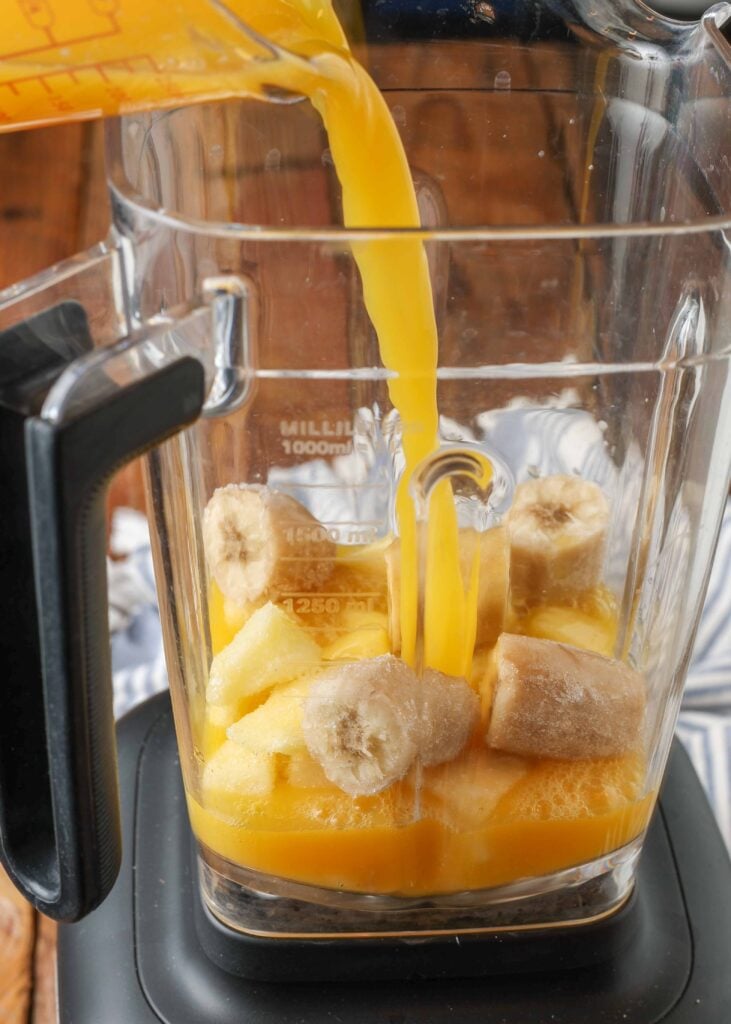 Pouring orange juice into blender with bananas and pineapple