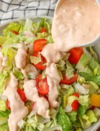 Salad dressing poured over fresh salad with tomatoes and bell peppers