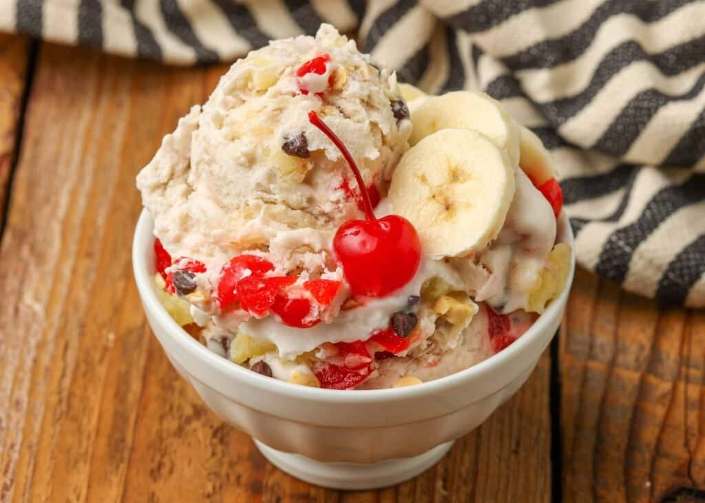 scoop of banana ice cream in white dish with whipped cream and a cherry on top