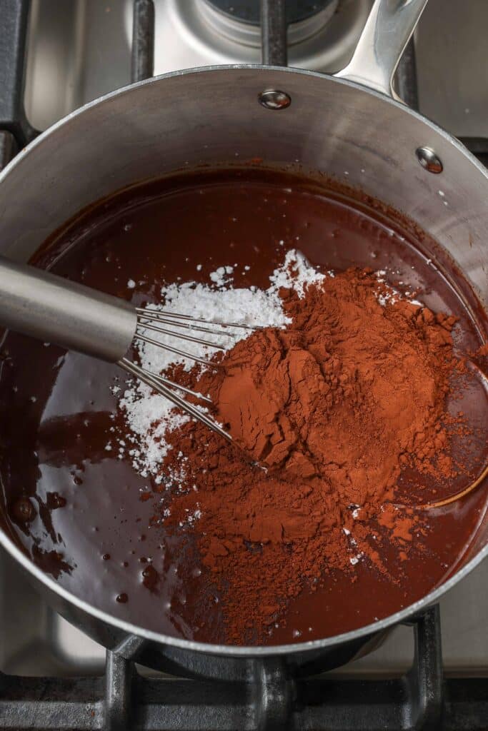 adding cocoa powder and sugar to chocolate in saucepan