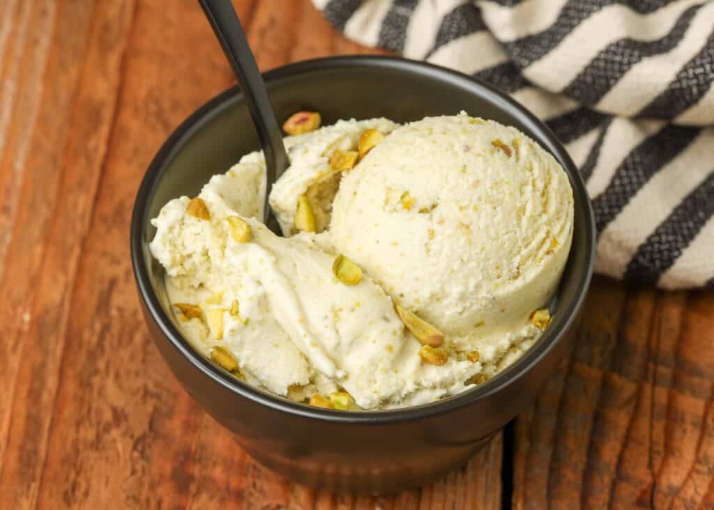 scoop of ice cream with pistachios in small black bowl