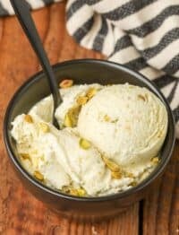 close up of pistachio ice cream in black dish with black spoon on wooden table