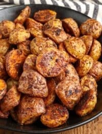 close up of roasted potatoes in black bowl next to black and white towel