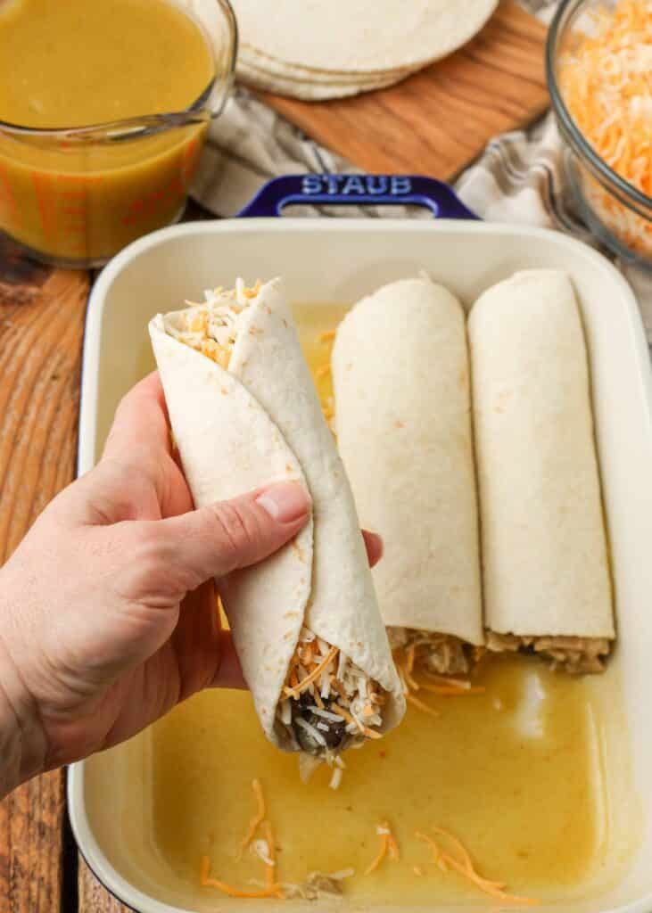 Rolling tortillas filled with chicken and black bean enchiladas