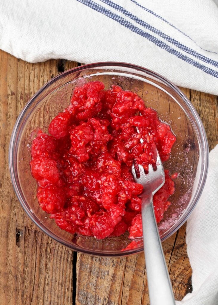 Mashed raspberries and sugar in glass bowl