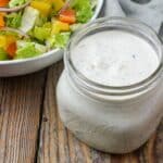 close up overhead photo of creamy salad dressing in jar next to salad