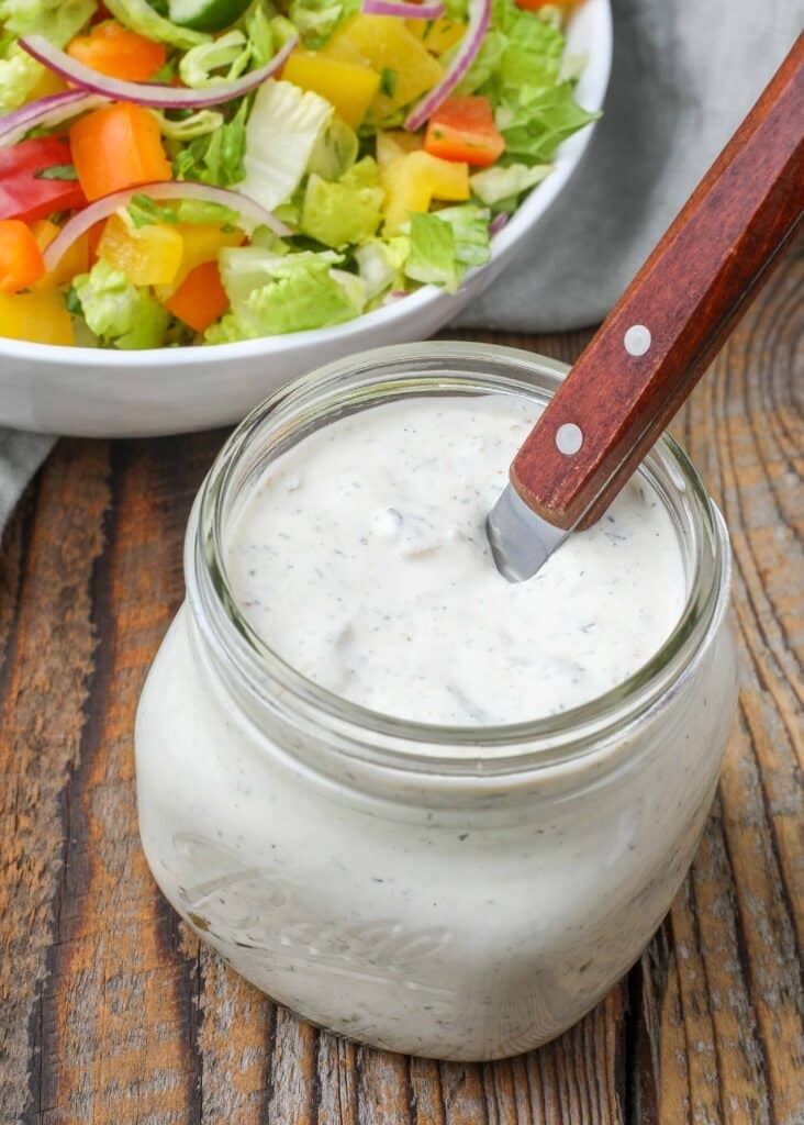 green chile ranch dressing in jar with spoon next to salad bowl