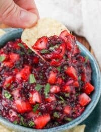 blueberry and strawberry salsa on a chip held by a hand over a blue bowl