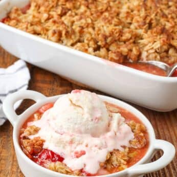 oat topped strawberry crisp in a white ceramic pan with an individual serving with ice cream on it.