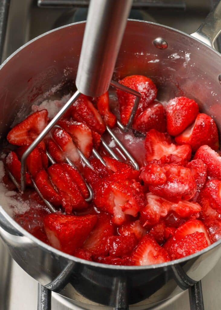 Using a potato masher to mash fresh strawberries in a pan