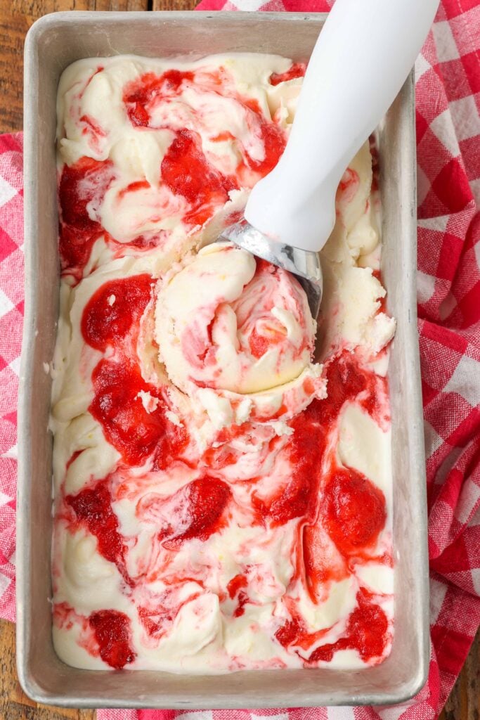 lemonade ice cream in a bread pan swirled with strawberry sauce with an ice cream scoop in the ice cream