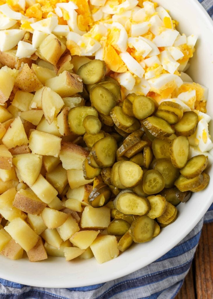 close up of dill pickles, potatoes, and hard boiled eggs in white bowl