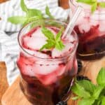 cocktail glass containing blackberries muddled in a bourbon smash on a cutting board with a blue checked napkin
