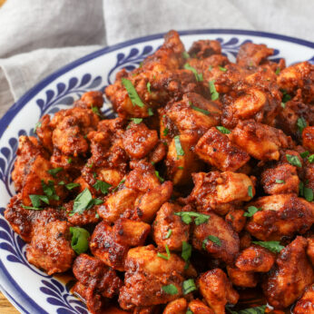 A vertically aligned photo of crispy chicken on a plate with a grey tea towel visible in the background.