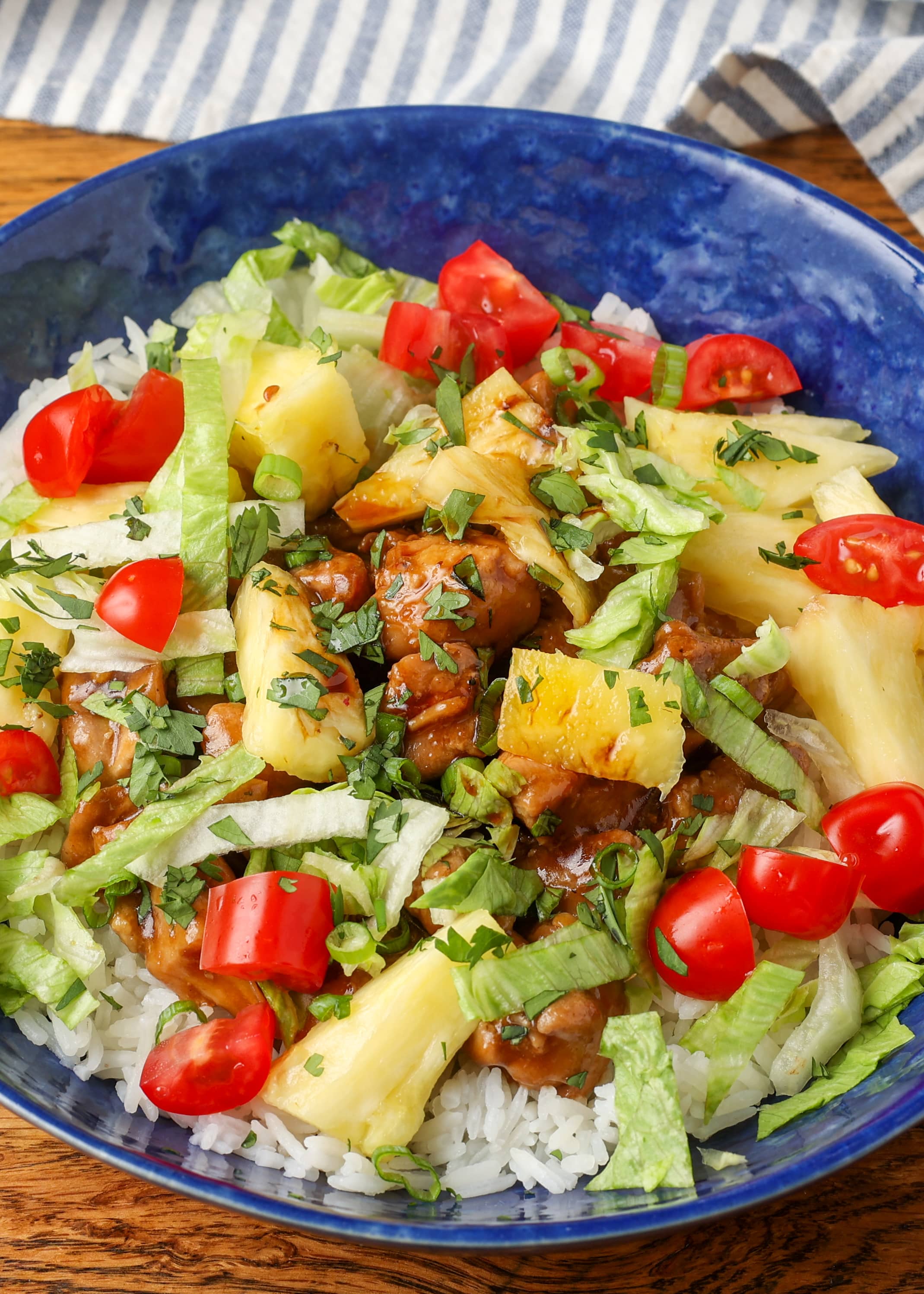 A vertically aligned shot of a Pineapple Teriyaki Chicken Bowl with a striped towel in the background.