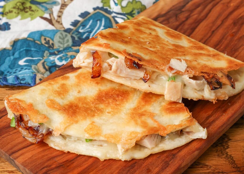 A close up horizontally aligned picture of caramelized onion chicken quesadillas with a colorful tea towel visible in the background. - 1