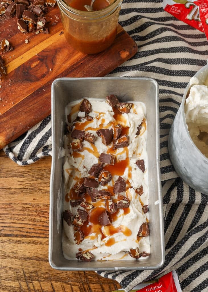 A top down image of a freezer safe tin full of turtle ice cream on a wooden tabletop with a black and white tea towel visible.