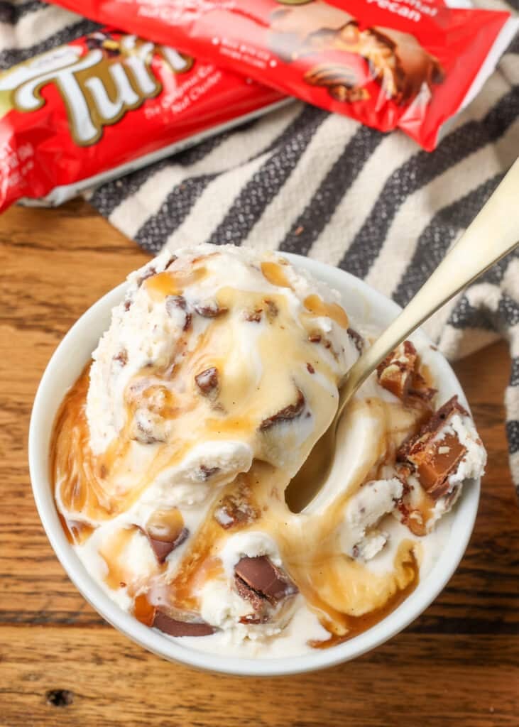 A close up shot of a serving of turtle ice cream in a ceramic bowl on a wooden tabletop with a striped tea towel visible in the background.