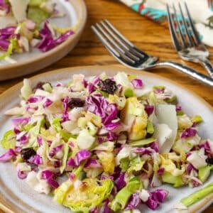 A vertically aligned close up shot of a serving of cabbage salad on a plate with a floral tea towel in the background.
